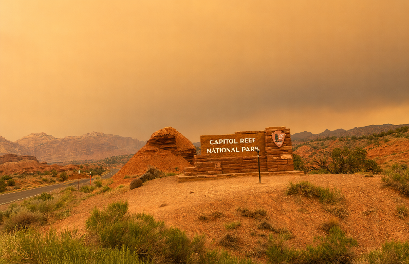Capitol Reef National Park entrance sign under smoky skies caused by nearby wildfires in Utah.